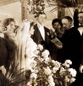 Photograph of couple being married, surrounded by friends and family