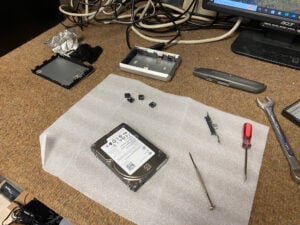 Photograph of an opened hard drive surrounded by tools and computer equipment